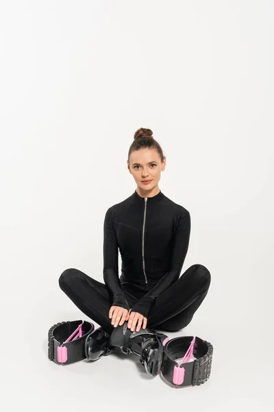 Boots for jumping, sportswoman in black jumpsuit sitting with crossed legs, kangoo jumping, — Stock Photo