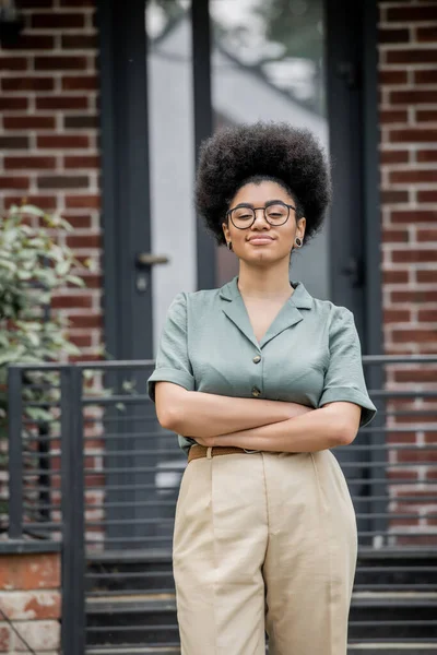 Sorridente mediatore immobiliare afroamericano in piedi con le braccia piegate vicino a un edificio moderno in città — Foto stock