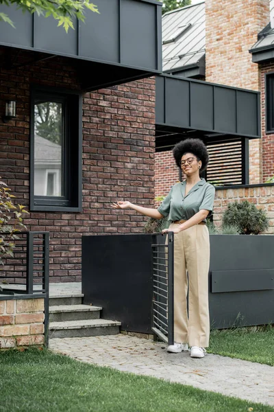 Heureux courtier immobilier afro-américain pointant avec la main et montrant chalet de la ville — Photo de stock