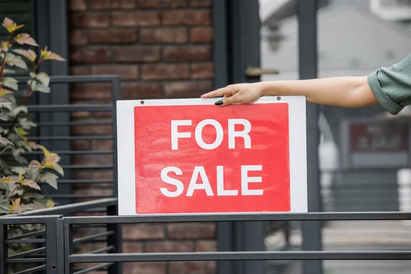 Vista ritagliata di afro-americano immobiliare in possesso di cartello con in vendita lettering vicino alla recinzione della casa — Foto stock