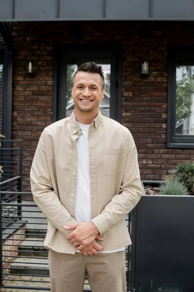 Joyful and successful property agent looking at camera near cottage on street — Stock Photo