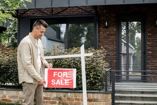 Agente immobiliare appeso cartello con per la vendita lettering vicino cottage moderno in città — Foto stock