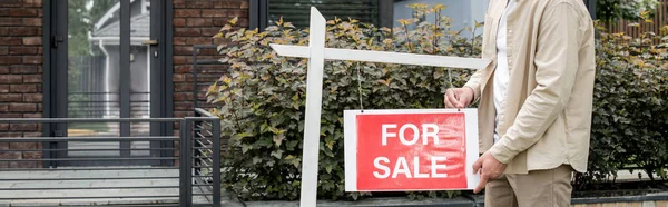 Cropped view of property realtor hanging for sale signboard near contemporary city house, banner — Stock Photo