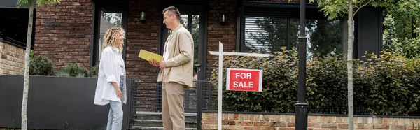 Agent immobilier positif parler au client près de la maison, plantes et à vendre enseigne sur la rue, bannière — Photo de stock