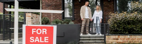 Nouveaux propriétaires se tenant la main et se regardant près de maison neuve et moderne sur la rue de la ville, bannière — Photo de stock