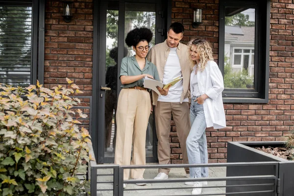 Smiling african american real estate agent showing documents to smiling owners of new house in city — Stock Photo