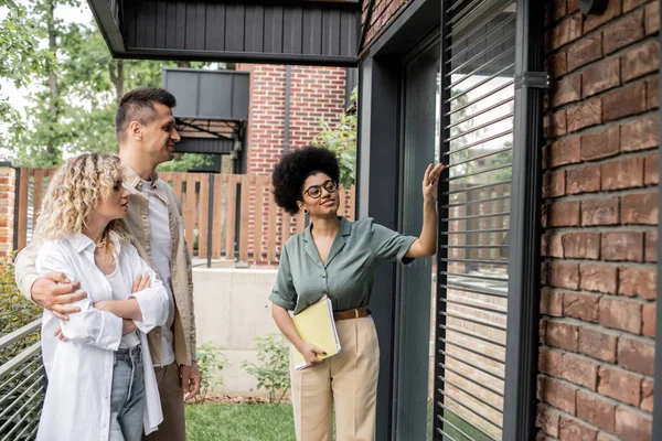 Corredor de bienes raíces afroamericano satisfecho con los documentos que muestran nueva casa de campo a los clientes - foto de stock