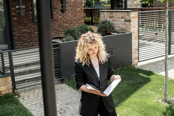 Blondine Immobilienmaklerin studiert Dokumente in Ordner neben modernem Haus zum Verkauf an der Stadtstraße — Stockfoto