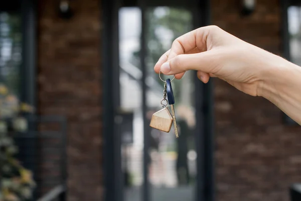 Partial view of real estate agent holding key near new city cottage on blurred background — Stock Photo