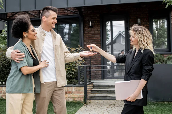 Delighted interracial couple taking key from new cottage from real estate broker on urban street — Stock Photo