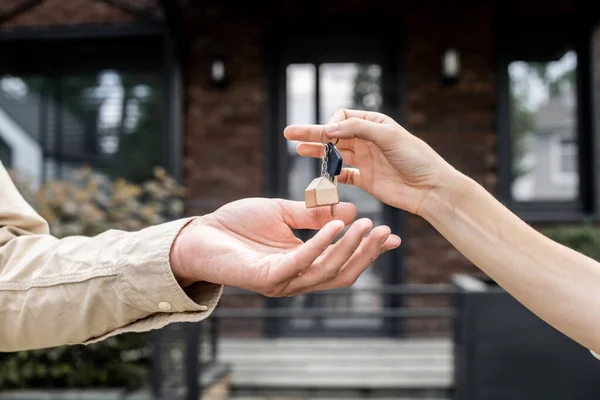 Partial view of property realtor giving key to client near city building on blurred background — Stock Photo