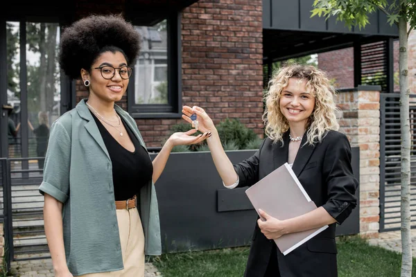 Agent immobilier blonde donnant la clé de la nouvelle maison à l'acheteur afro-américain heureux — Photo de stock