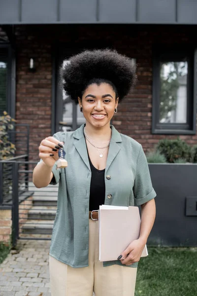 Feliz e bem sucedido corretor imobiliário afro-americano com pasta segurando chave perto de nova casa de campo — Fotografia de Stock