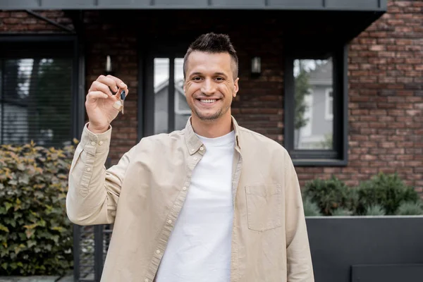 Overjoyed real estate agent holding key from new house and smiling at camera, property business — Stock Photo