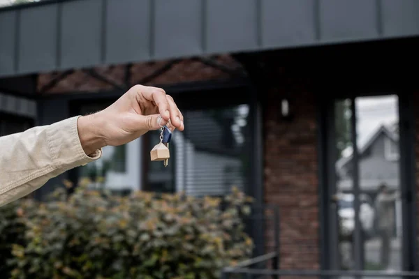 Partial view of professional property agent holding key near modern cottage on blurred background — Stock Photo