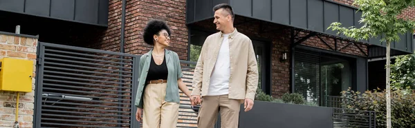 Vista parziale della coppia multietnica che si tiene per mano vicino a nuova casa di città, nuova vita, proprietari felici — Foto stock