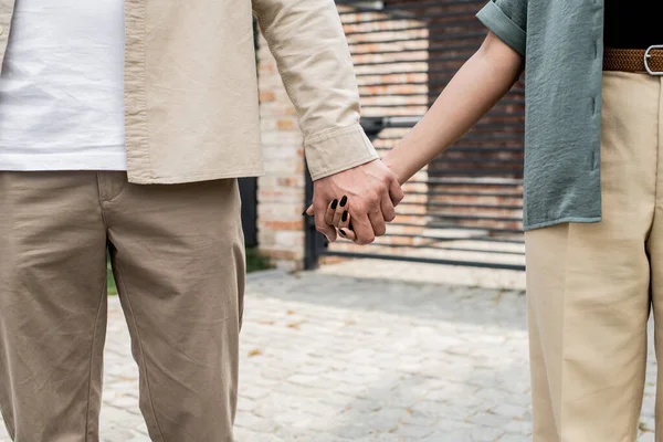 Overjoyed multicultural property owners holding hands and smiling at each other near new house — Stock Photo