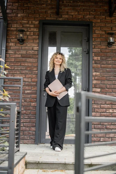 Full length of stylish and confident realtor standing with folder near new house in city — Stock Photo