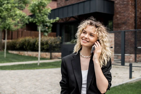 Smiling property realtor looking away while talking on smartphone near building on city street — Stock Photo