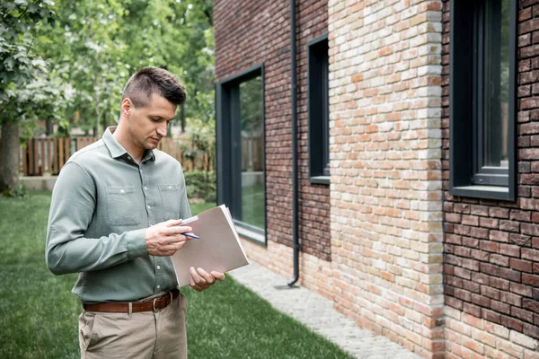 Real estate agent holding folder and pen while standing near contemporary building on city street — Stock Photo