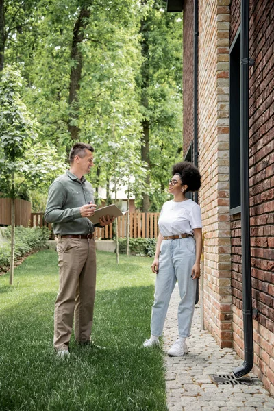 Comprimento total de agente imobiliário confiante conversando com mulher afro-americana perto de edifício na rua — Fotografia de Stock