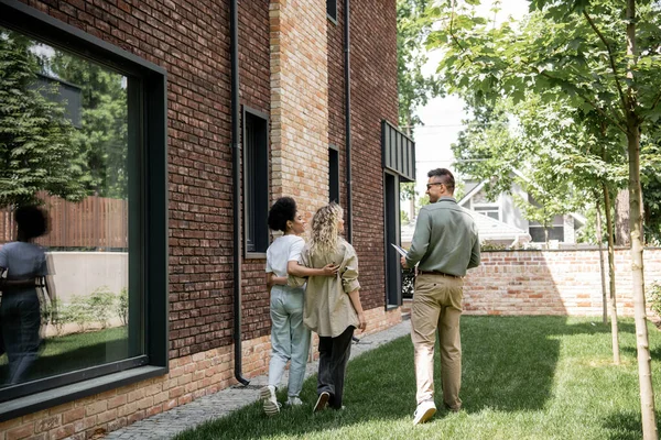 Comprimento total de casal lésbico interracial e corretor imobiliário andando ao longo de nova casa de campo na rua — Fotografia de Stock