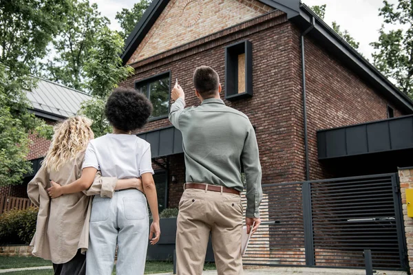 Back view of real estate broker showing new cottage to interracial lesbian couple outdoors — Stock Photo