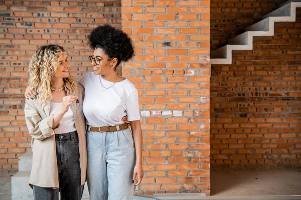 Glückliche multiethnische Frauen mit Schlüsseln aus der neuen Wohnung, die einander umarmen und anschauen — Stockfoto