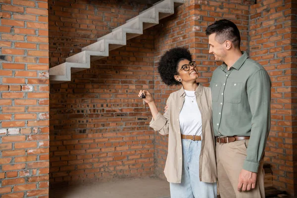 Overjoyed african american woman holding keys and looking at man in new own house — Stock Photo