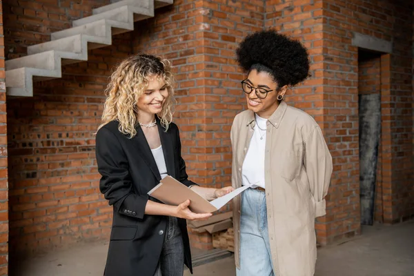 Smiling real estate agent showing documents to african american client in new house — Stock Photo