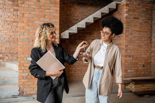 Real estate agent with folder giving keys from new house to overjoyed african american client — Stock Photo