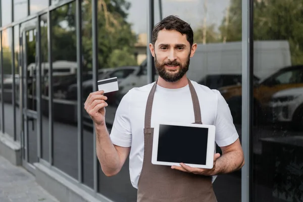 Smiling barista holding credit card and digital tablet with blank screen on urban street — Stock Photo