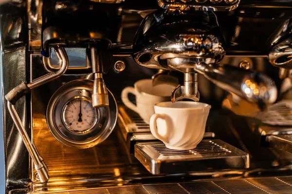 Vista de perto do café derramando da máquina de café em copo branco com luz solar no café, extração — Fotografia de Stock