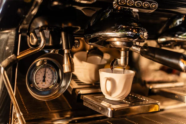 Vista de cerca del café que vierte de la máquina en taza blanca en la luz del sol en la cafetería - foto de stock