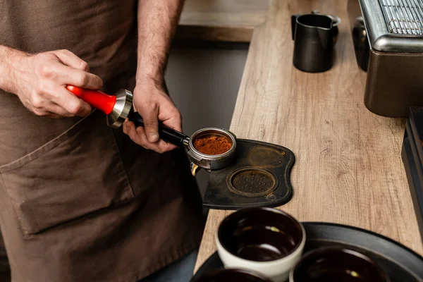Cropped view of barista in apron holding holder with coffee in coffee shop — Stock Photo