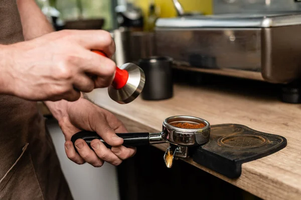 Cropped view of barista in apron holding press and holder with coffee in coffee shop — Stock Photo