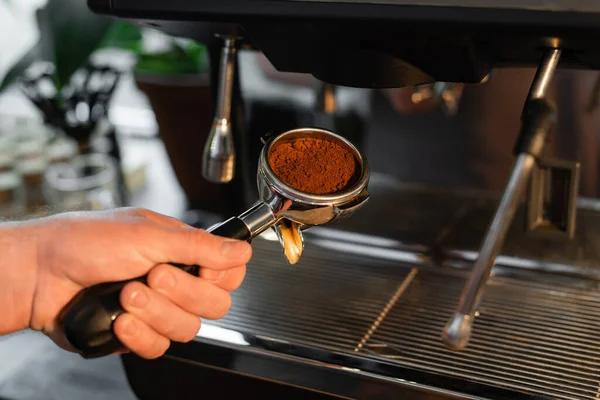 Vista cortada de barista segurando titular com café perto de máquina de café borrada no café — Fotografia de Stock