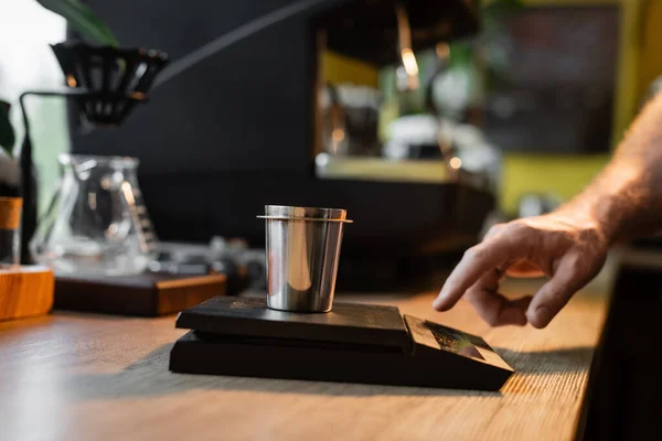 Vista cortada de barista usando balanças eletrônicas e copo perto de máquina de café borrada no café — Fotografia de Stock
