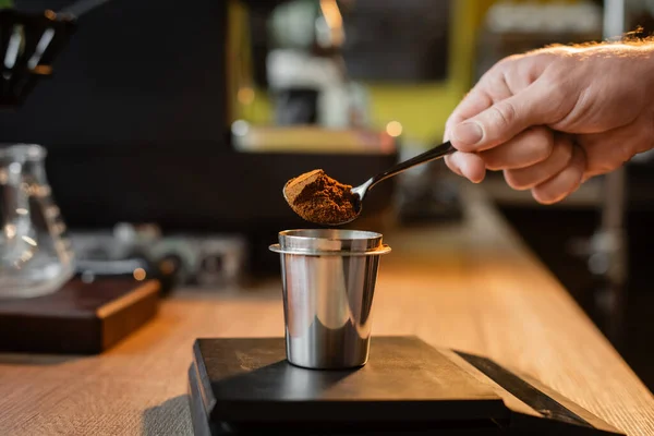 Vista ritagliata di barista con cucchiaio versando caffè in becher su bilance elettroniche in caffetteria — Foto stock