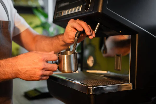 Cropped view of barista frothing milk in pitcher on coffee machine while working in coffee shop — Stock Photo