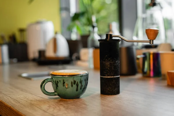 Mühle mit Gewürzen in der Nähe einer Tasse Cappuccino auf Arbeitsplatte im Café im Hintergrund — Stockfoto