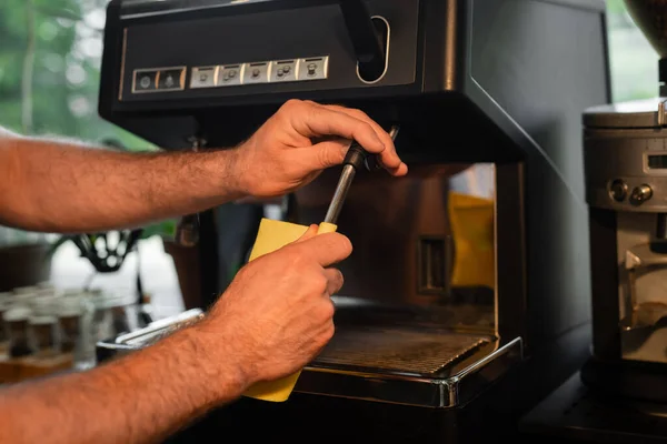 Vista recortada de barista con trapo limpieza de la boquilla de la máquina de café mientras trabaja en la cafetería - foto de stock