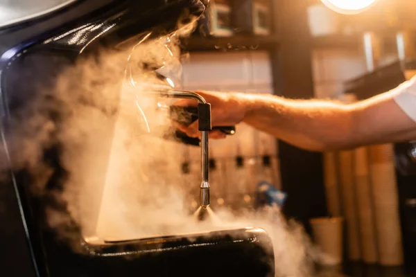 Vista recortada de barista en delantal usando cafetera cerca de vapor e iluminación en cafetería - foto de stock