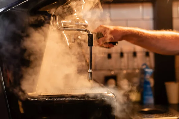 Vista cortada de barista desfocado usando máquina de café com vapor e iluminação no café — Fotografia de Stock