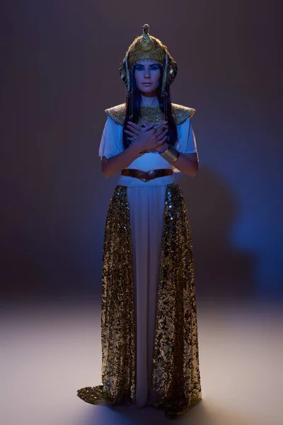 Volle Länge einer Frau in ägyptischer Kleidung, die auf braunem Hintergrund mit blauem Licht in die Kamera blickt — Stockfoto