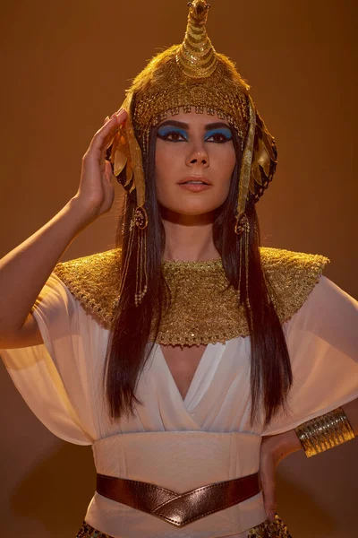 Портрет брюнетки в єгипетському вбранні тримає руку на стегні на коричневому фоні з тіні — стокове фото