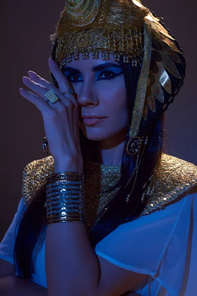 Portrait of beautiful woman in Egyptian headdress posing in blue light on brown background — Stock Photo