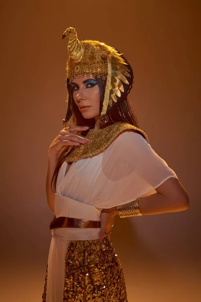 Elegante donna in look egiziano e copricapo guardando la fotocamera su sfondo marrone — Foto stock
