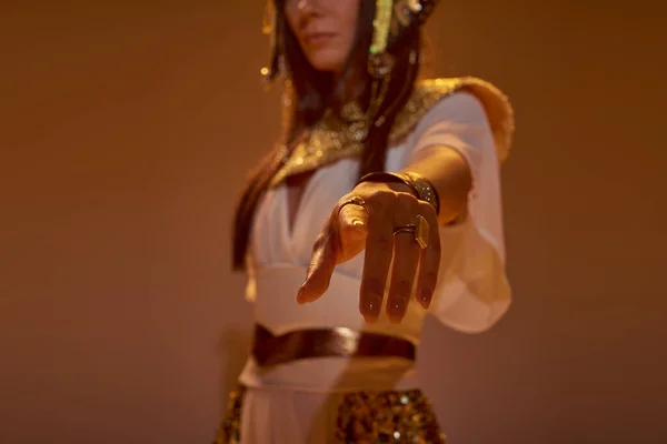 Обрізаний вид розмитої жінки в єгипетському вбранні, що вказує пальцем на камеру на коричневому фоні — стокове фото
