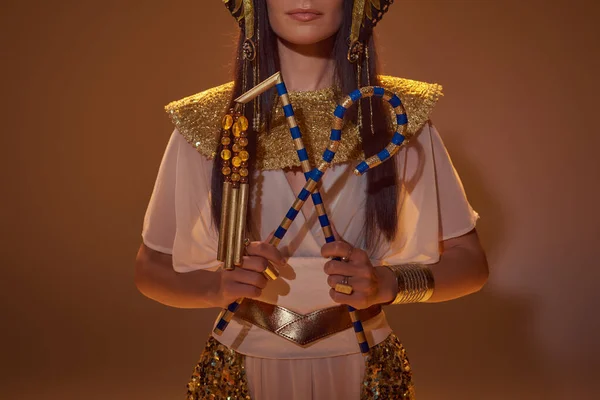 Vista ritagliata della donna in sguardo egiziano tenendo truffatore e flagello su sfondo marrone — Foto stock